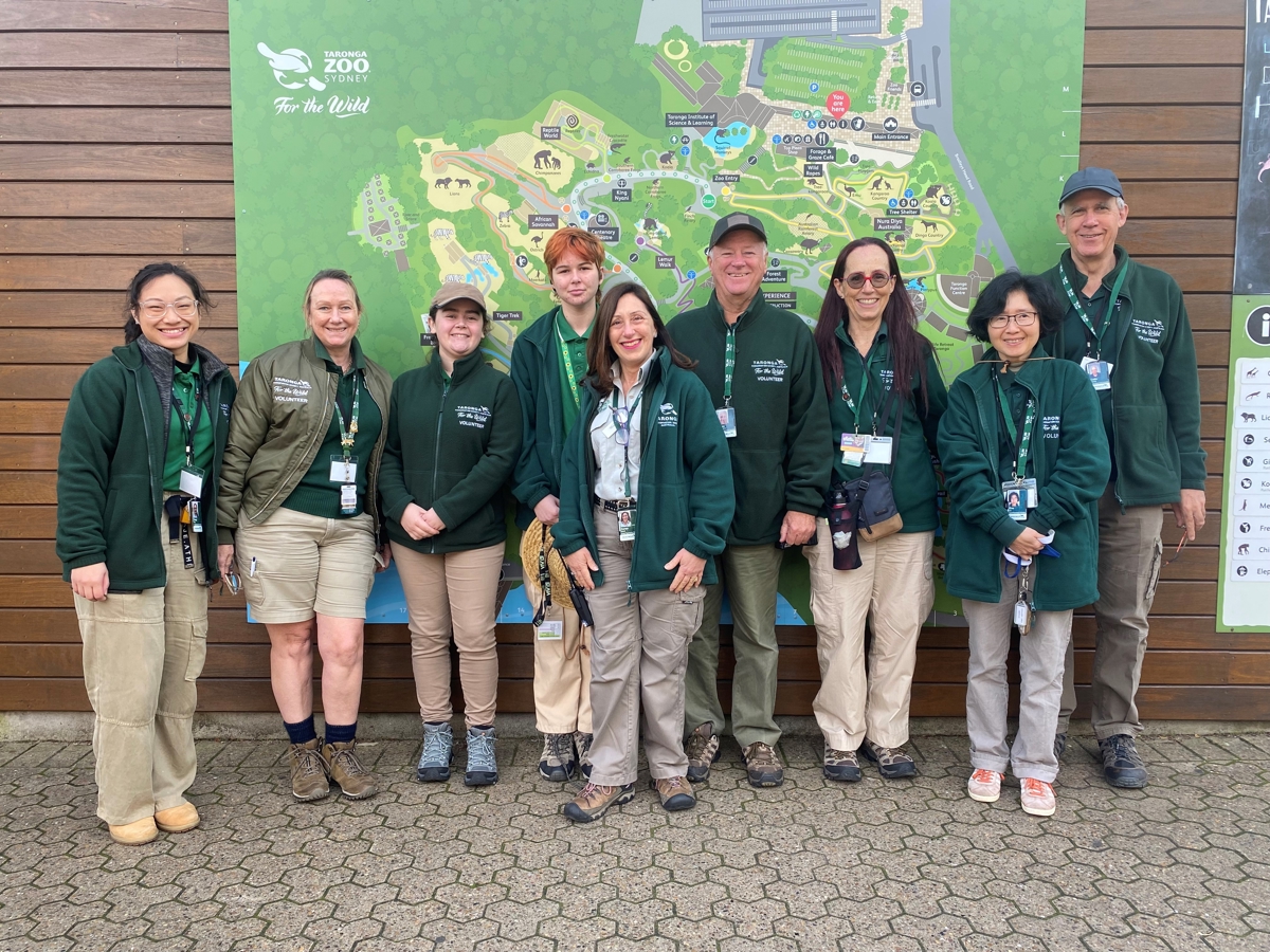 A group of Guest Experience Volunteers standing in front of the zoo map