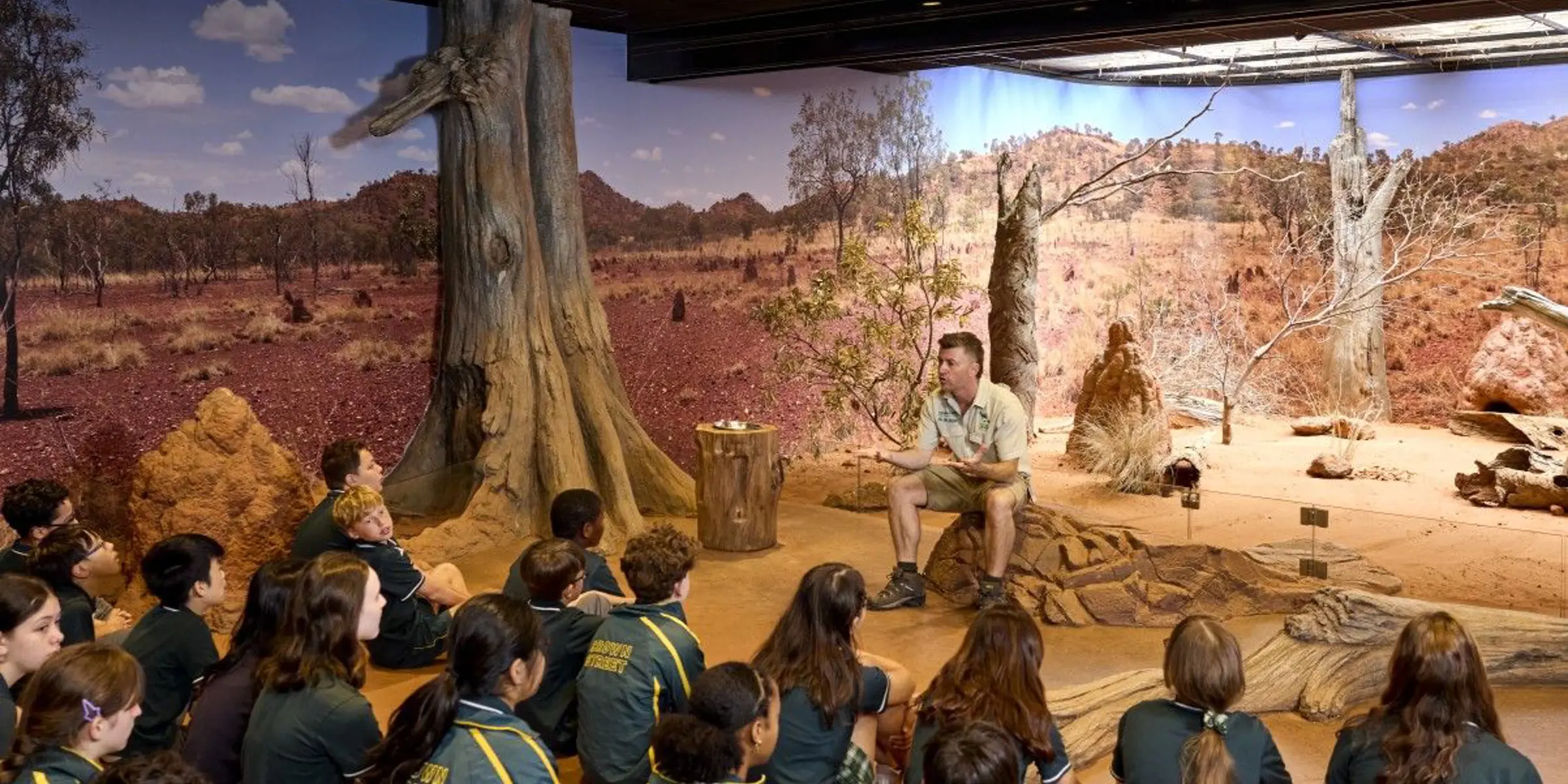 School students seated indoors listening to a guide in a desert-themed immersive classroom.