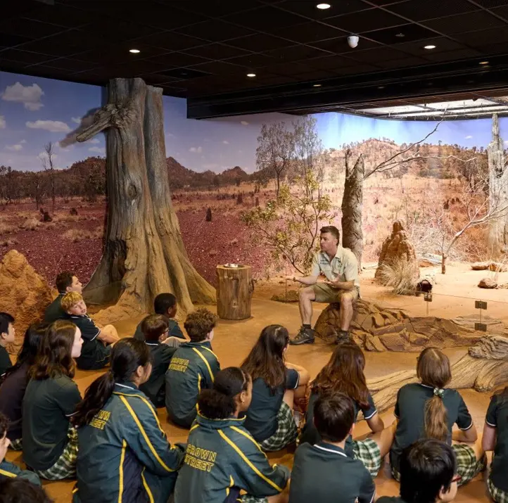 School students seated indoors listening to a guide in a desert-themed immersive classroom.