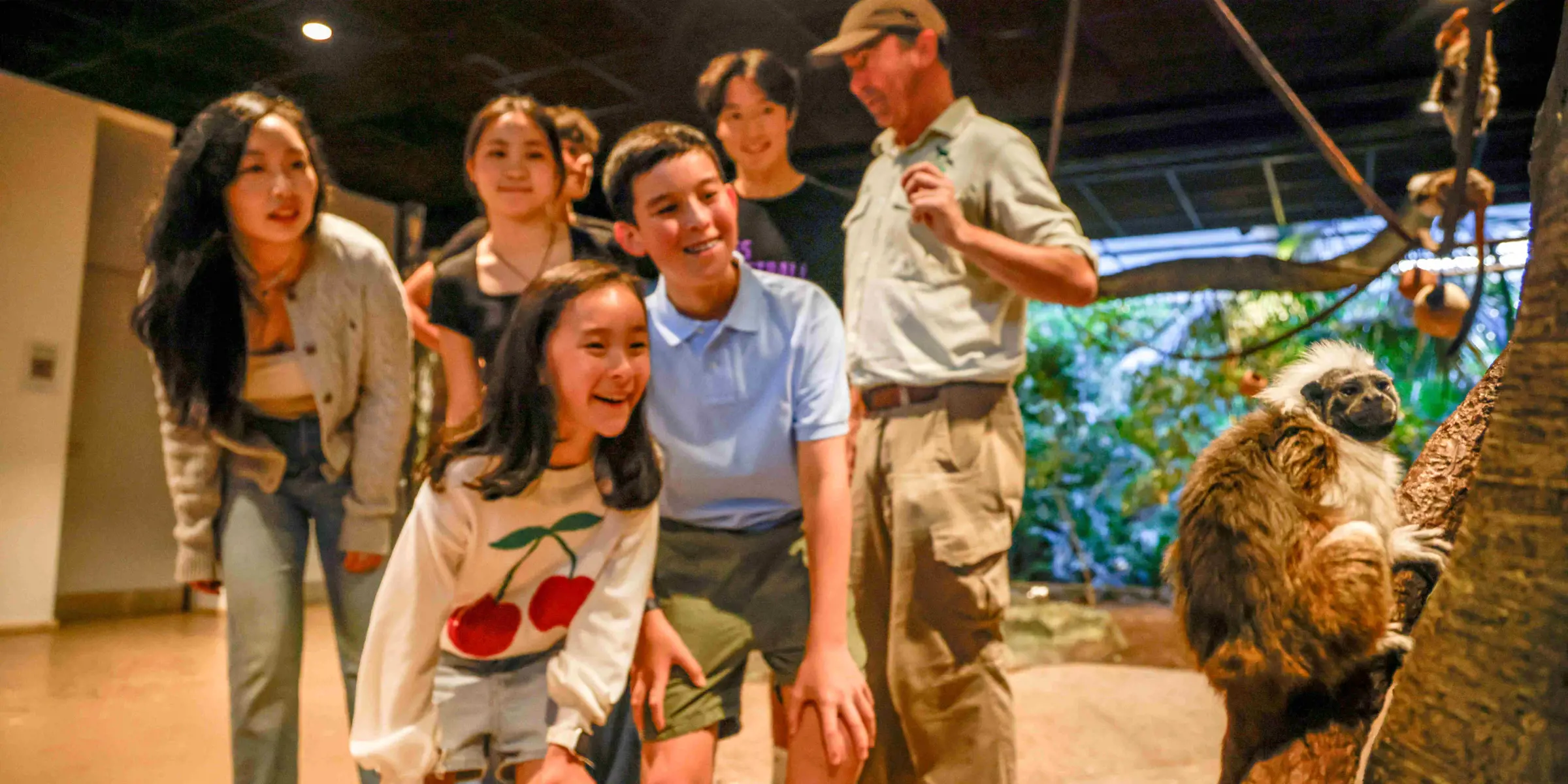 School students observing a monkey climbing in an immersive classroom while an educator stands nearby.