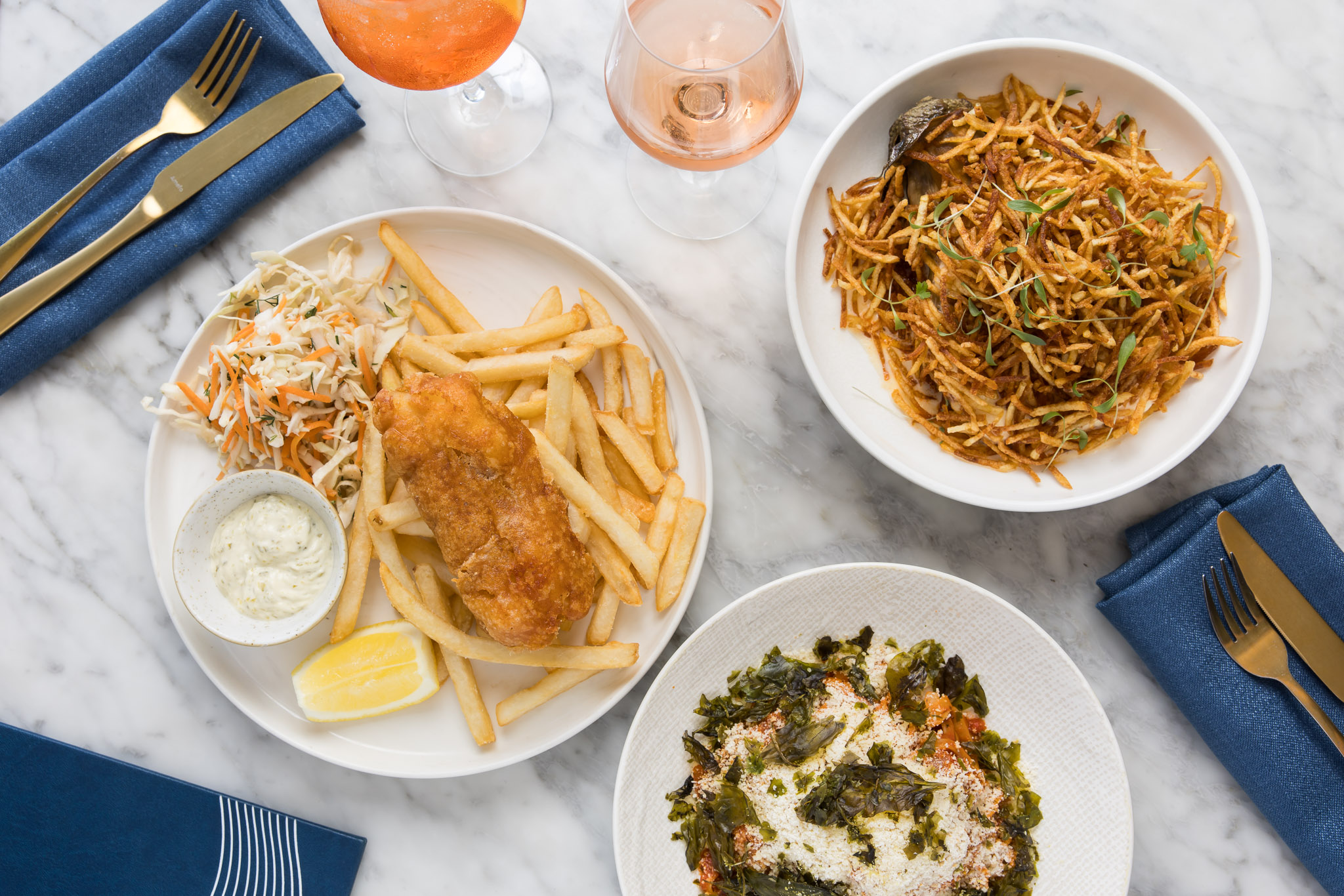 Plates of fish and chips, pasta and salad seen from above on a marble table.