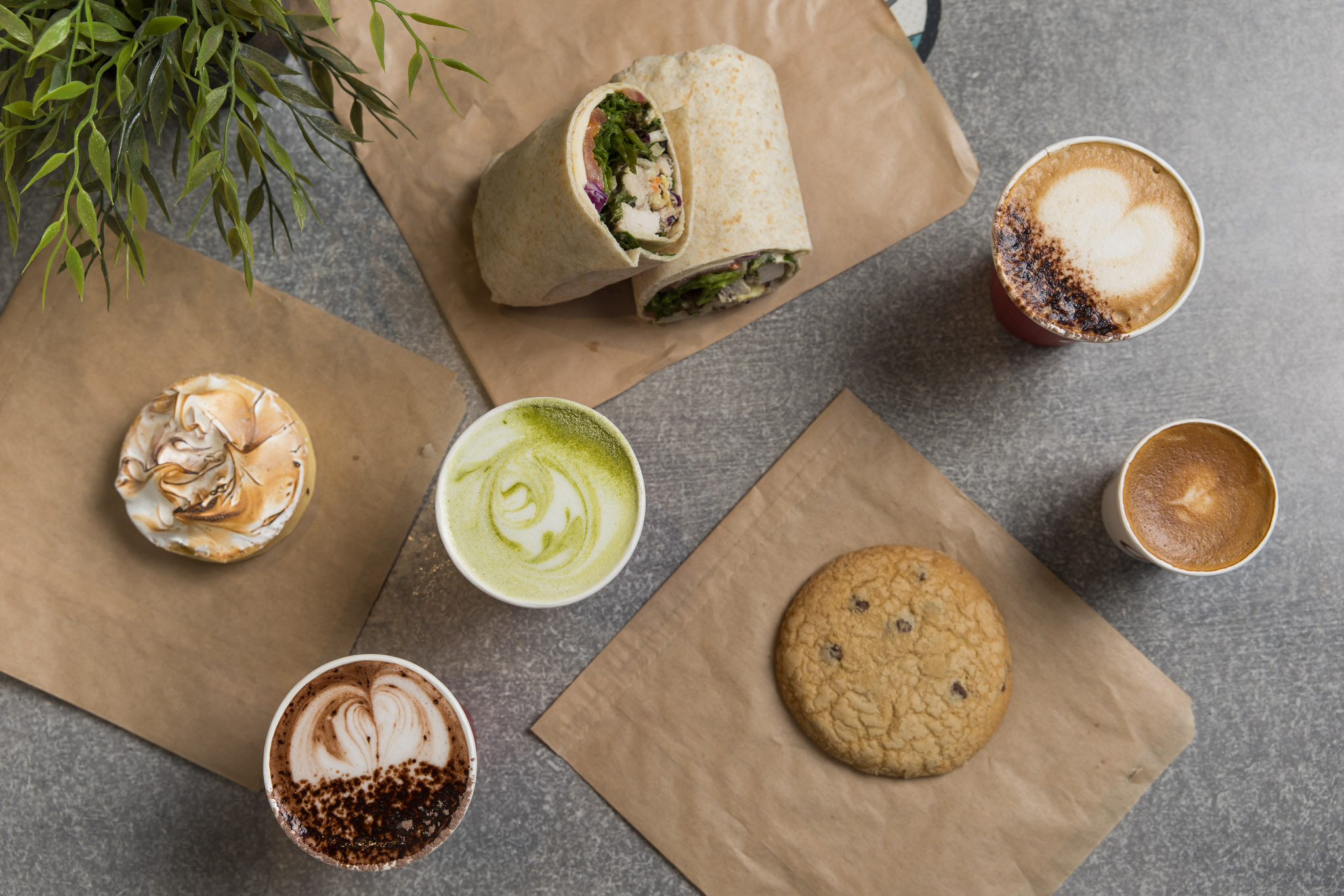 Coffee, matcha, a wrap and a cookie on a café table.
